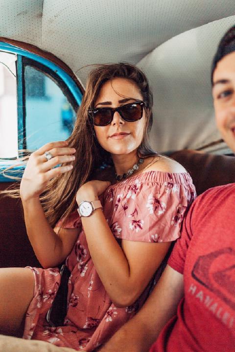 Woman in sunglasses and a pink floral dress riding in the back seat of a vintage car in Cuba