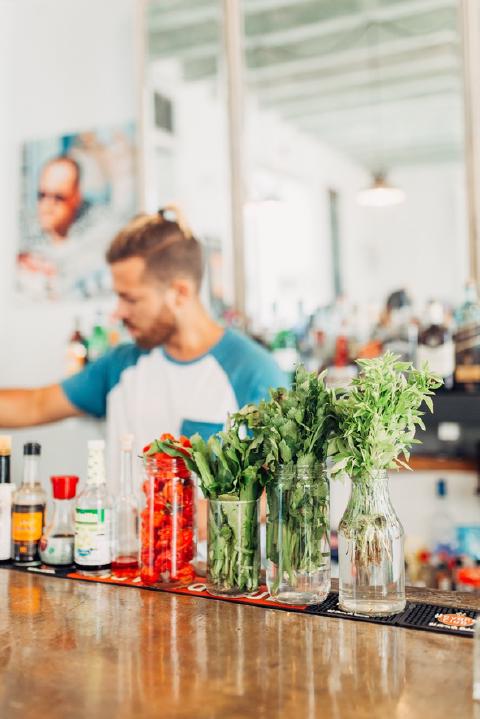 Jars of herbs and peppers lining a Havana bar counter, with the bartender blurred behind them