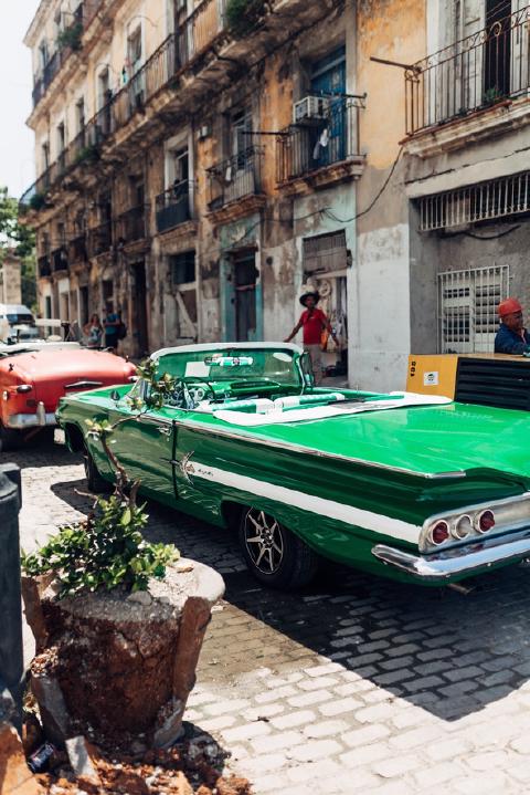 Green-and-white classic convertible parked on a cobbled Havana street below weathered balconied facades