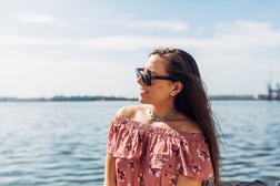 A woman in sunglasses and a floral off-shoulder top looks out over the water along a Cuban seafront