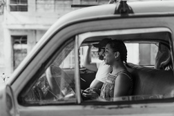 Black-and-white view through the window of a classic car in Cuba, a couple sitting together in the back seat