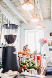 Coffee grinders and trays of limes on a bar counter under pendant lamps in a white-beamed Cuban cafe
