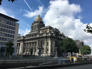 Massive ornate stone courthouse with a scaffolded gold dome rising over a Brussels boulevard with tram tracks
