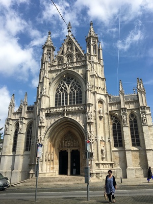 Gothic church facade in Brussels with pointed spires and a carved arched portal, a woman walking past on the sidewalk