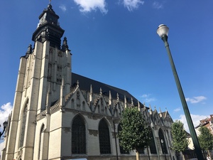 Stone Gothic church with a dark rounded bell tower under a deep blue Brussels sky, a tall street lamp beside it