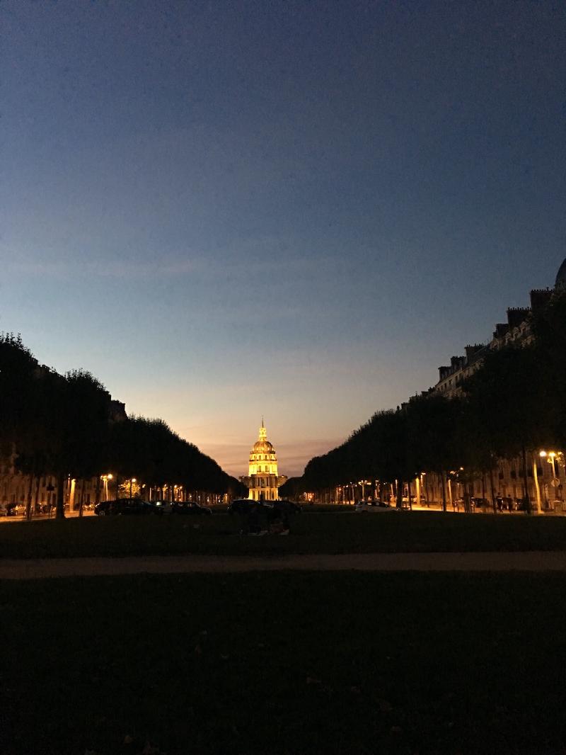 The golden dome of Les Invalides glows at dusk at the end of a tree-lined grassy avenue in Paris