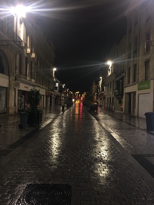 Empty rain-slicked pedestrian shopping street in Caen at night, streetlights reflecting off the wet cobblestones