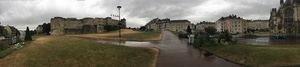 Panorama of a grassy park and paths under an overcast sky in Caen, old stone ramparts and row houses in the distance