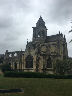Weathered medieval stone church with a square tower and partly ruined nave under gray skies in Caen