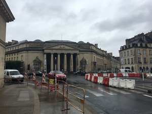 Neoclassical columned building in Caen behind orange construction barriers on a wet overcast street
