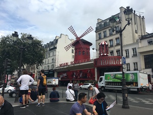 The red windmill of the Moulin Rouge overlooking a busy Paris square, tourists sitting and walking in the foreground