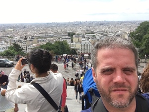 Selfie of a bearded man above crowded steps in Montmartre, the Paris skyline stretching out hazily below