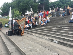 A harpist plays beside wide stone steps in Paris while onlookers sit along the stairway