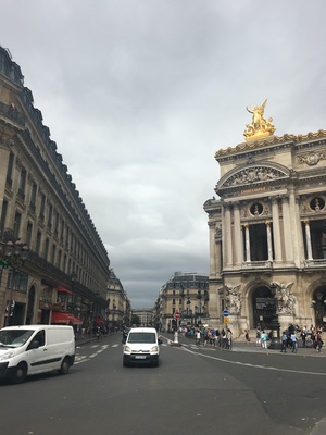 Vans drive past the ornate Palais Garnier opera house in Paris, a gilded statue atop its corner under grey skies