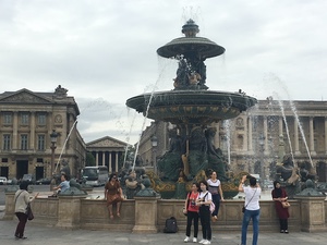 Tourists photograph each other before a tiered fountain with sculpted figures at Place de la Concorde in Paris