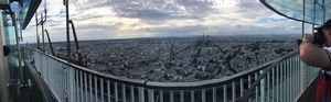 Panorama of the Paris cityscape from a fenced rooftop observation deck at dusk