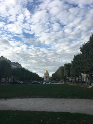 The gilded dome of Les Invalides at the end of a tree-lined lawn under dappled clouds in Paris