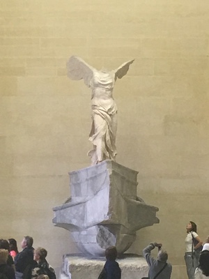 The Winged Victory of Samothrace atop its ship-prow pedestal at the Louvre, visitors gathered below