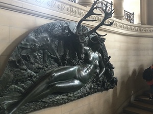 Bronze relief of a reclining stag with tall antlers mounted along a stone staircase in the Louvre