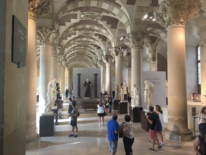 Visitors wander a long columned sculpture hall at the Louvre lined with white marble statues