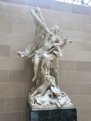 White marble sculpture group of intertwined figures on a pedestal in a skylit Louvre gallery