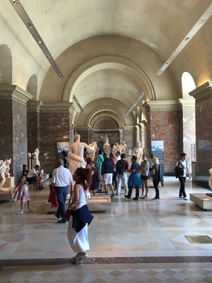 Visitors fill a vaulted Louvre gallery of classical marble statues lit by tall windows