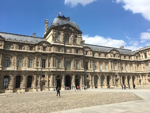 Ornate stone facade of the Louvre&rsquo;s Cour Carree courtyard under blue sky with scattered clouds