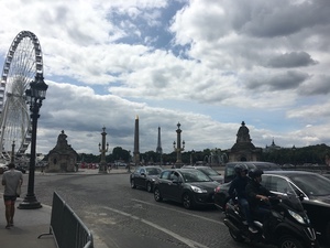 Traffic and a motorcyclist pass Place de la Concorde, with its obelisk and a Ferris wheel beyond