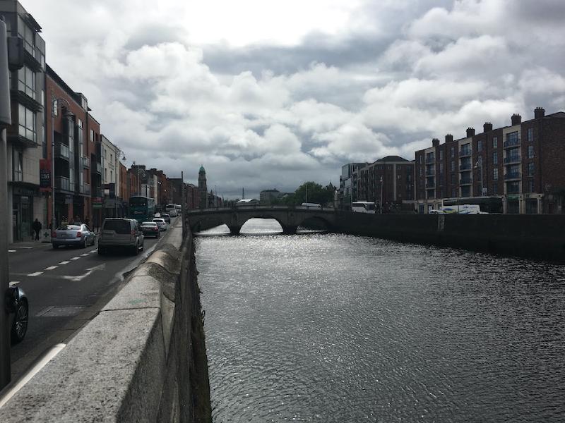 The River Liffey in Dublin sparkling under cloudy skies, an arched stone bridge and quayside traffic ahead