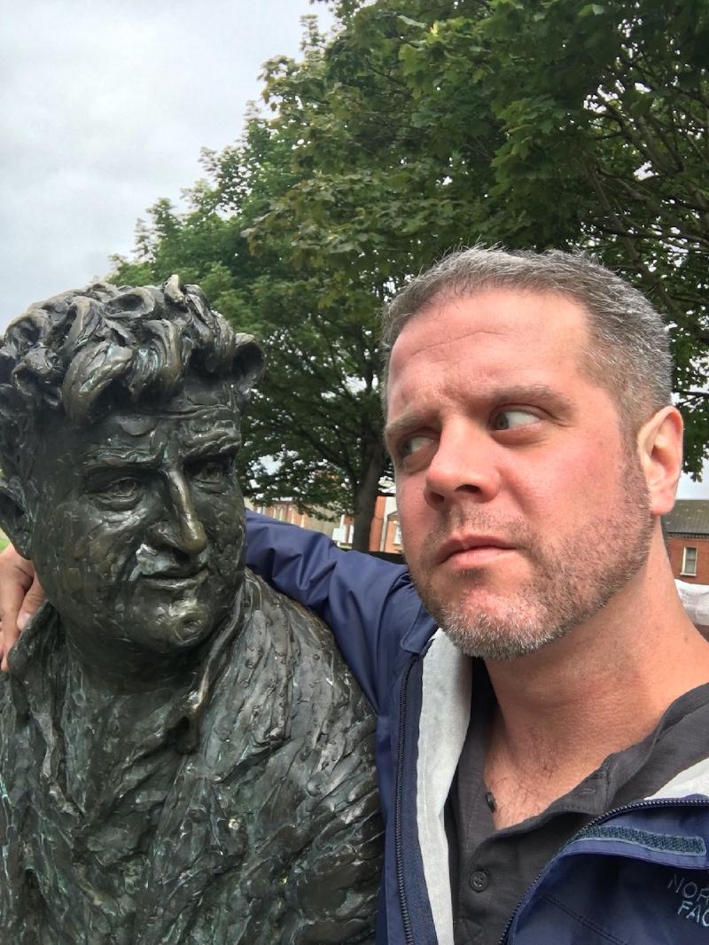 Selfie of a bearded man with his arm around a bronze statue of a tousle-haired man in Dublin