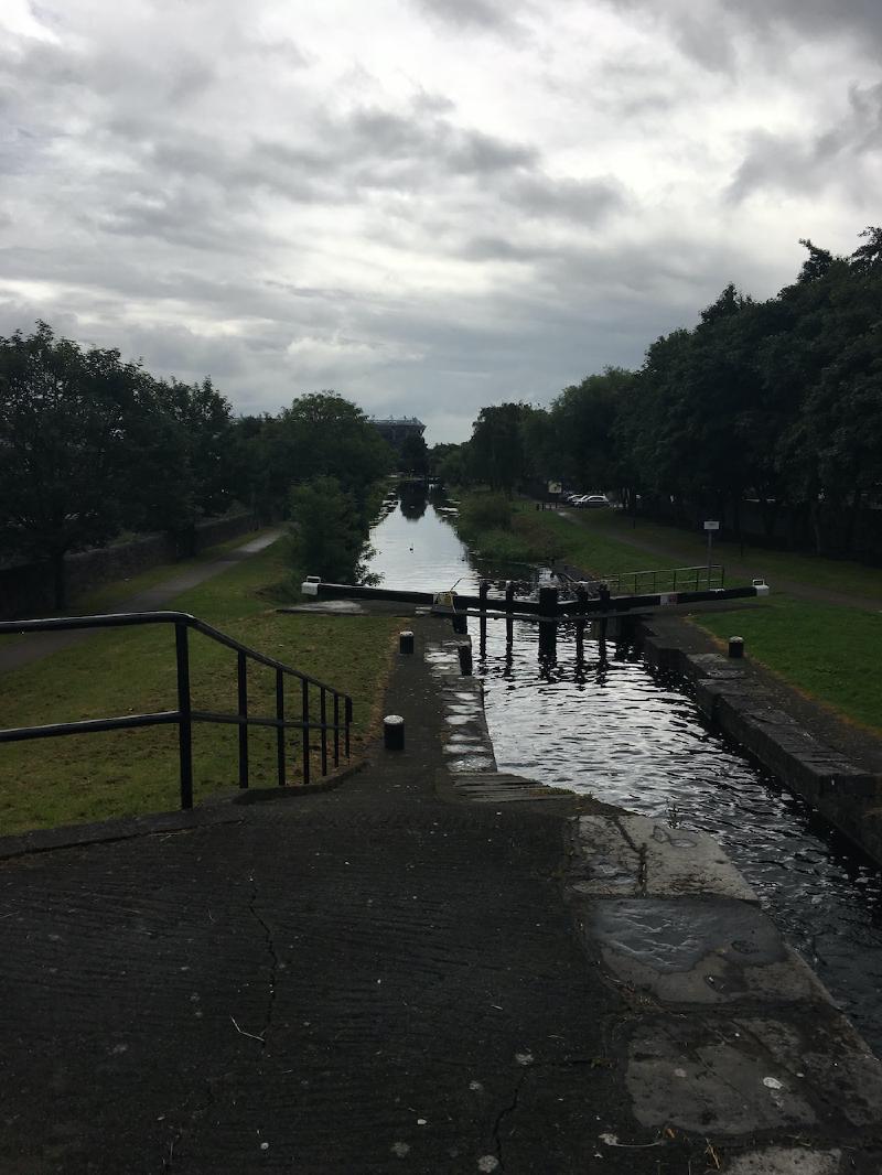 Canal lock gates on a tree-lined stretch of canal in Dublin under heavy grey clouds, a swan on the water