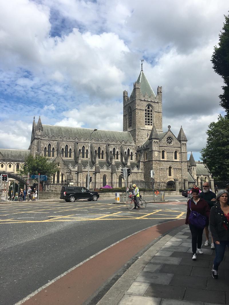 Christ Church Cathedral&rsquo;s stone tower rises over a Dublin street as pedestrians and a cyclist pass the crossing