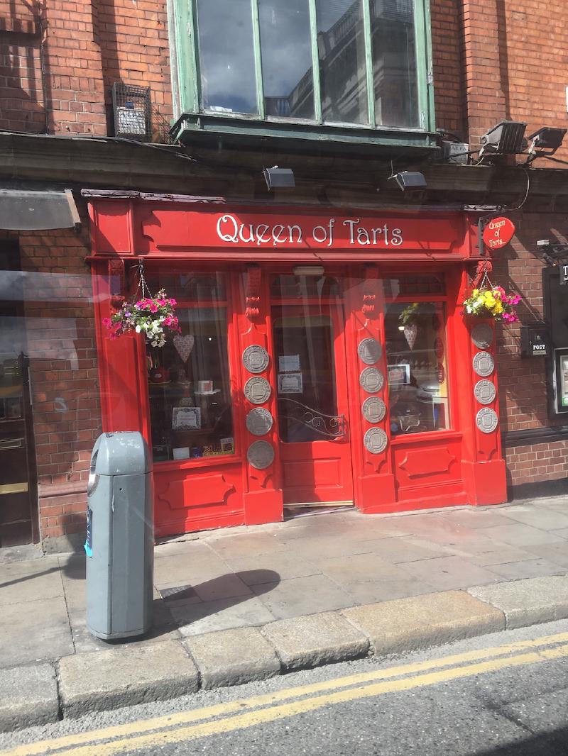 Bright red storefront of the Queen of Tarts bakery in Dublin, decorated with hanging flower baskets and award plaques