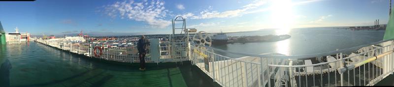 Panorama from a ferry&rsquo;s top deck leaving Dublin Port, with docks, cranes, and sunlit sea stretching to the horizon
