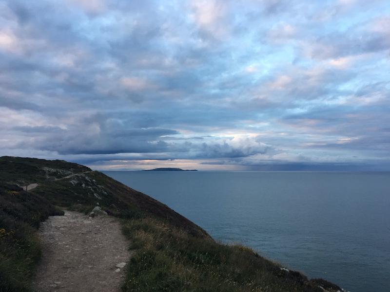 Dirt cliff path at Howth curving above the sea at dusk, a distant island under blue-gray clouds