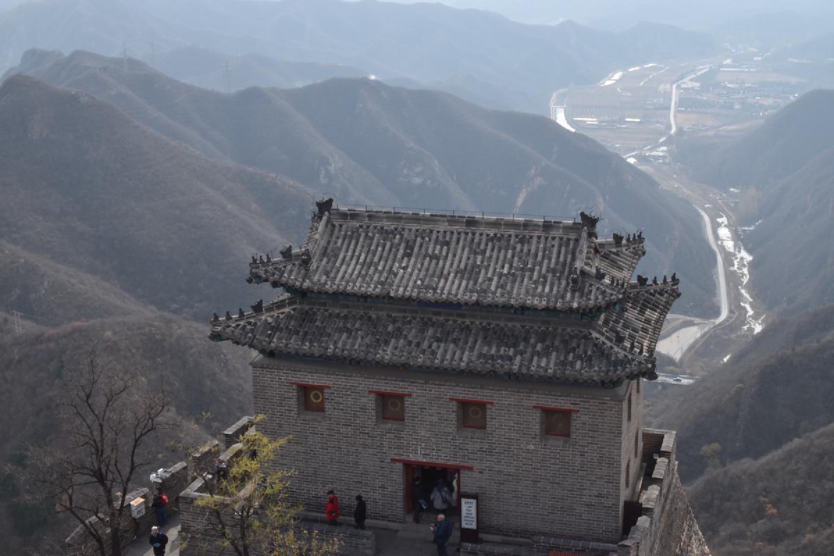 Double-roofed watchtower on the Great Wall overlooking a deep valley with a winding river and road