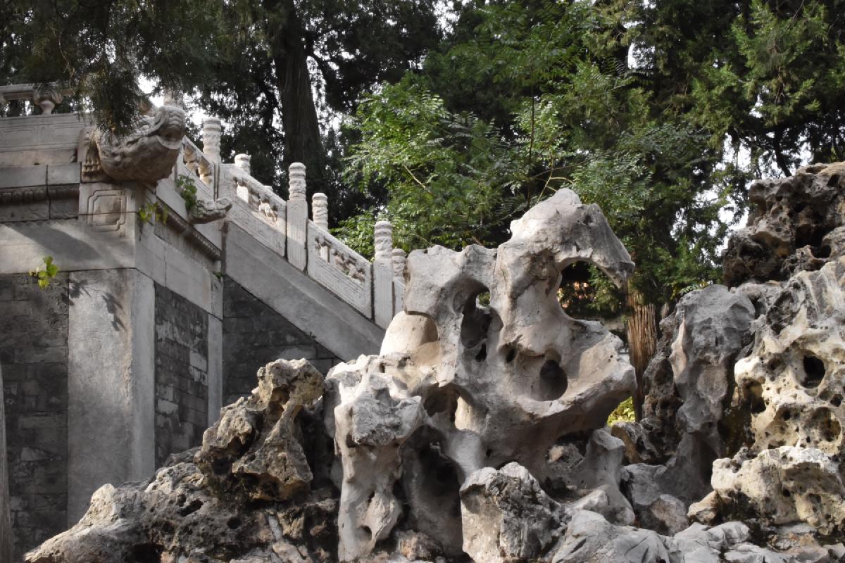 Weathered, hole-pocked scholar rocks beside a carved marble stairway in the Forbidden City&rsquo;s garden