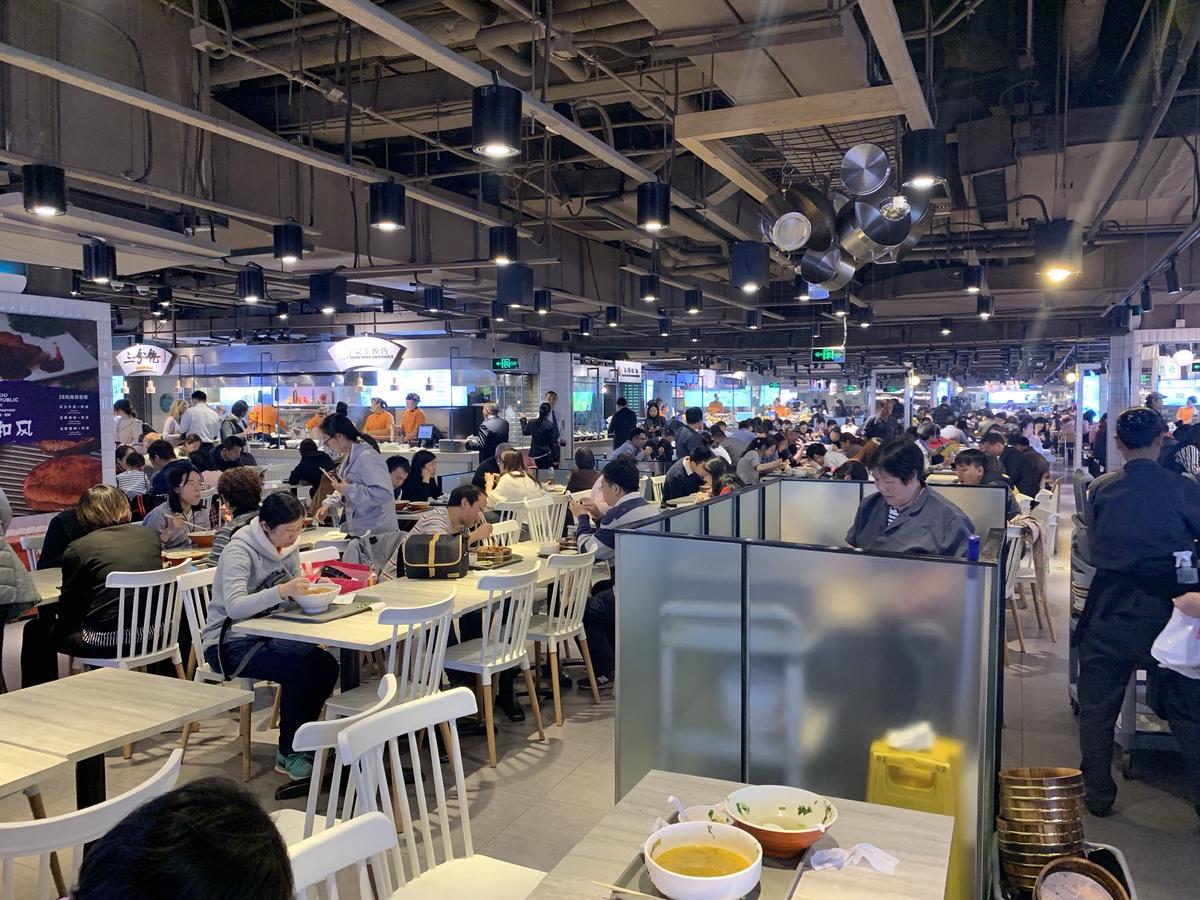 Busy food court crowded with diners at white tables under an open industrial ceiling in Beijing