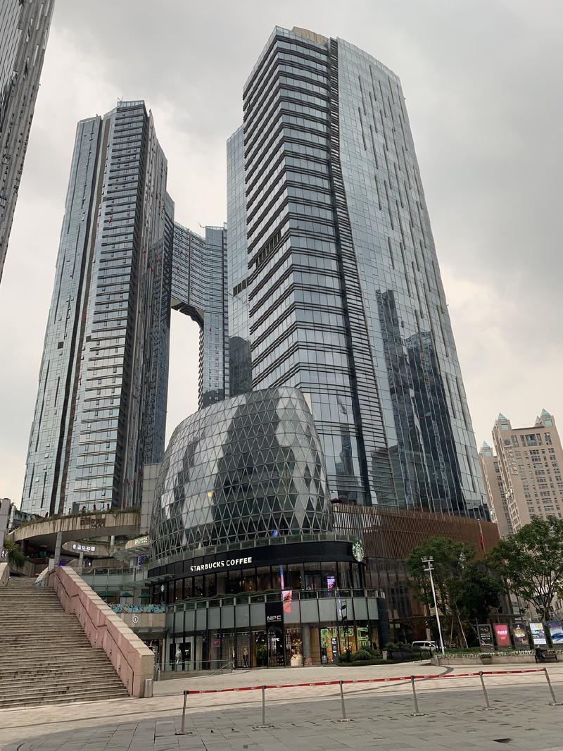 Glass towers rise above a domed shopping podium with a Starbucks at street level in Chengdu, China