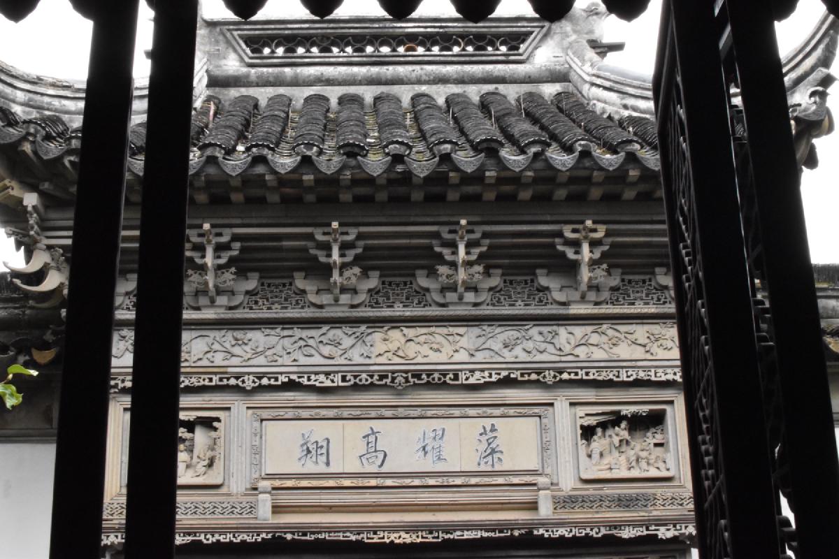 A tiled roof and carved stone gateway with an inscribed plaque, framed by dark pillars, Shanghai, China