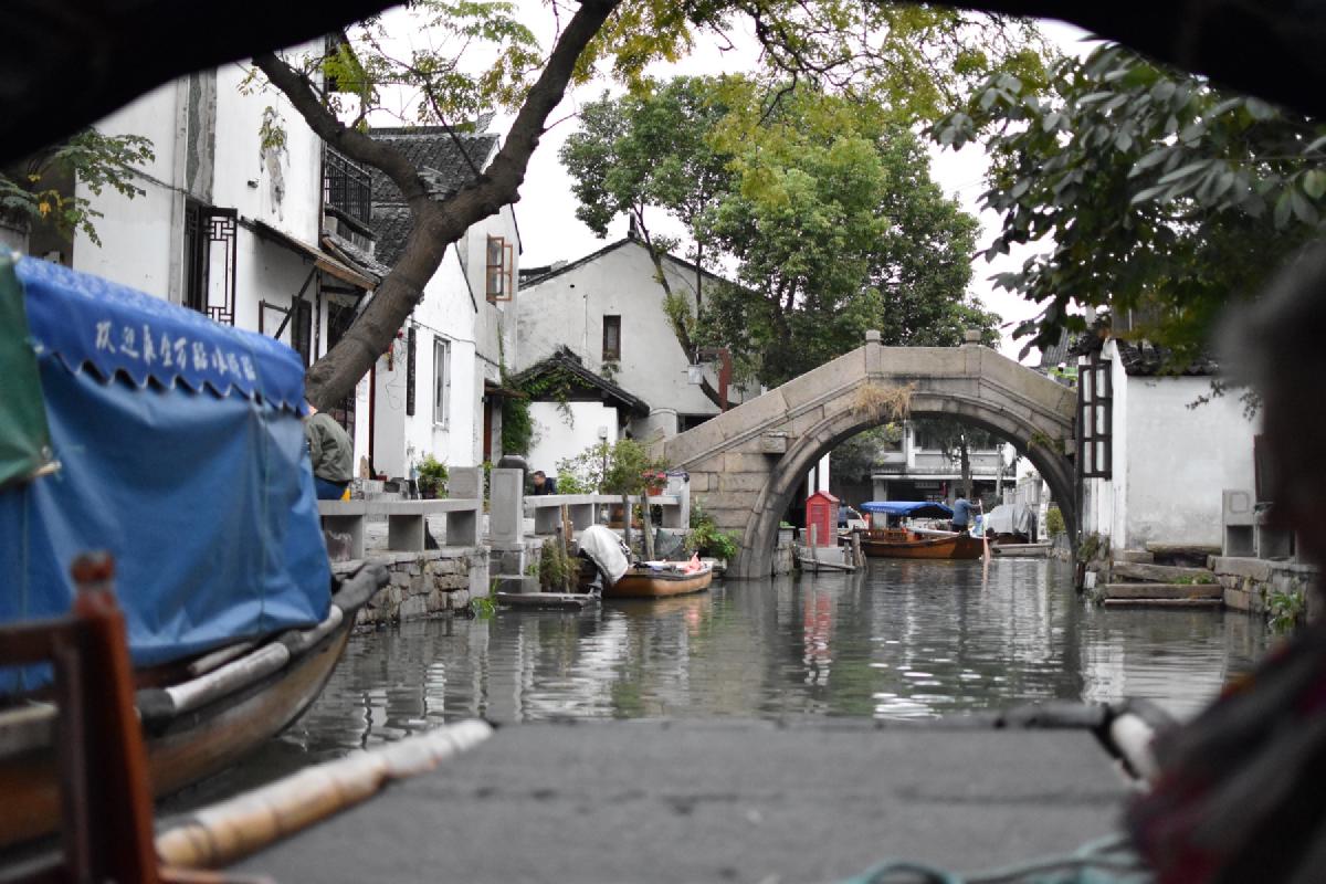 Blue-canopied wooden boats moored on a canal below a stone arch bridge and whitewashed houses in China
