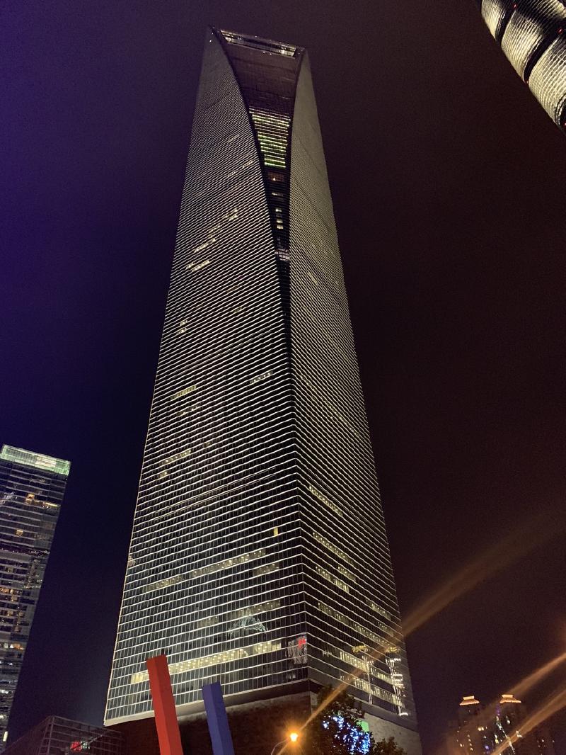 The Shanghai World Financial Center at night, its wedge-shaped tower and trapezoid opening seen from street level