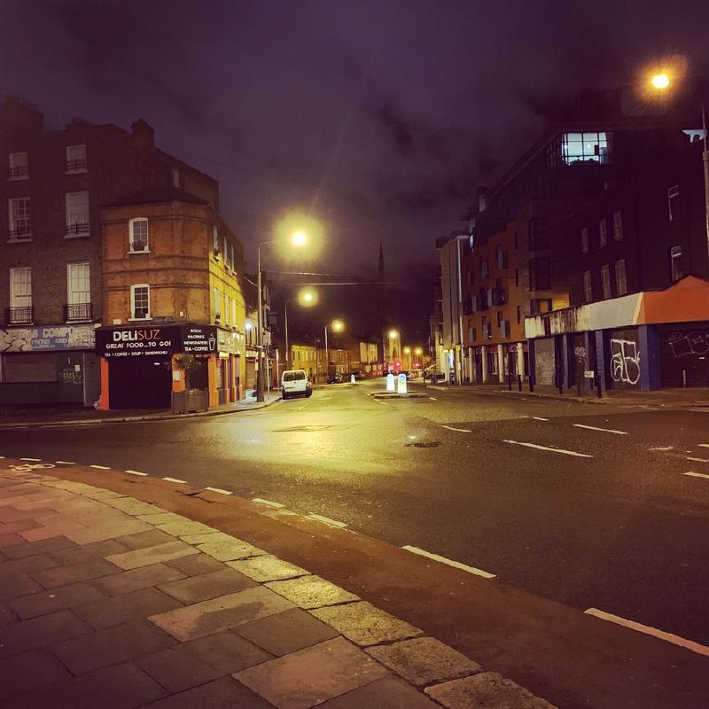 Empty Dublin street corner at night, a lit deli storefront and streetlights glowing over wet pavement