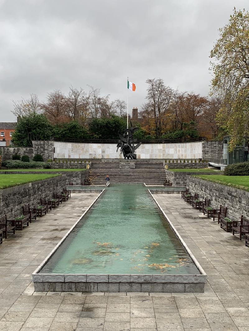 Long reflecting pool of the Garden of Remembrance in Dublin, benches along both sides and the Irish flag flying beyond