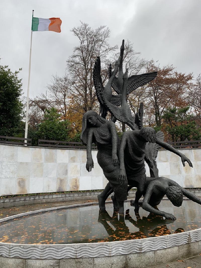 Children of Lir bronze sculpture of falling figures and rising swans above a leaf-strewn pool, Irish tricolor overhead