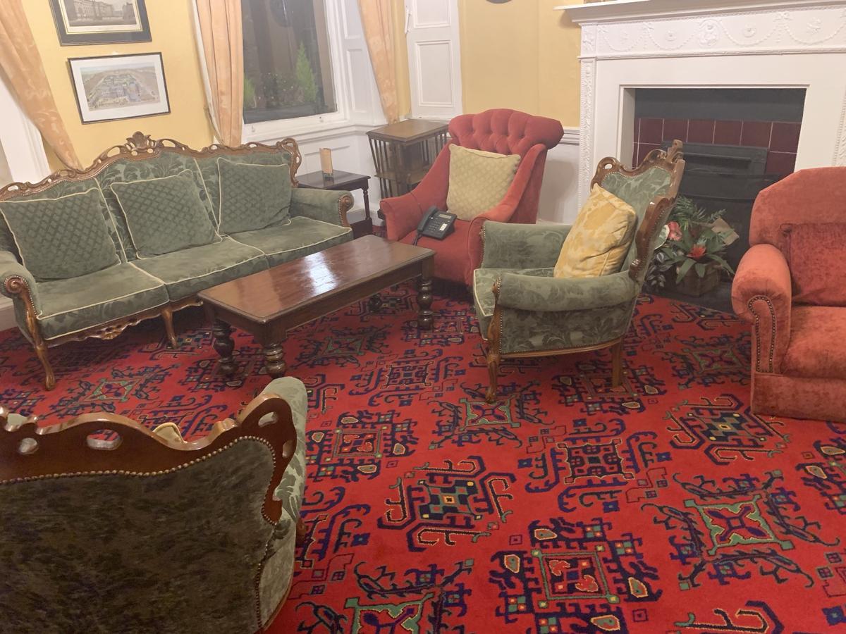 Old-fashioned hotel sitting room with green velvet couches, red armchairs, a marble fireplace, and patterned red carpet