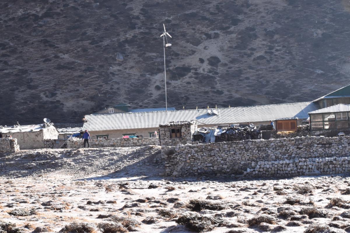 Stone-walled trekking lodge with a small wind turbine in a frosty Himalayan village in Nepal, hillside looming behind