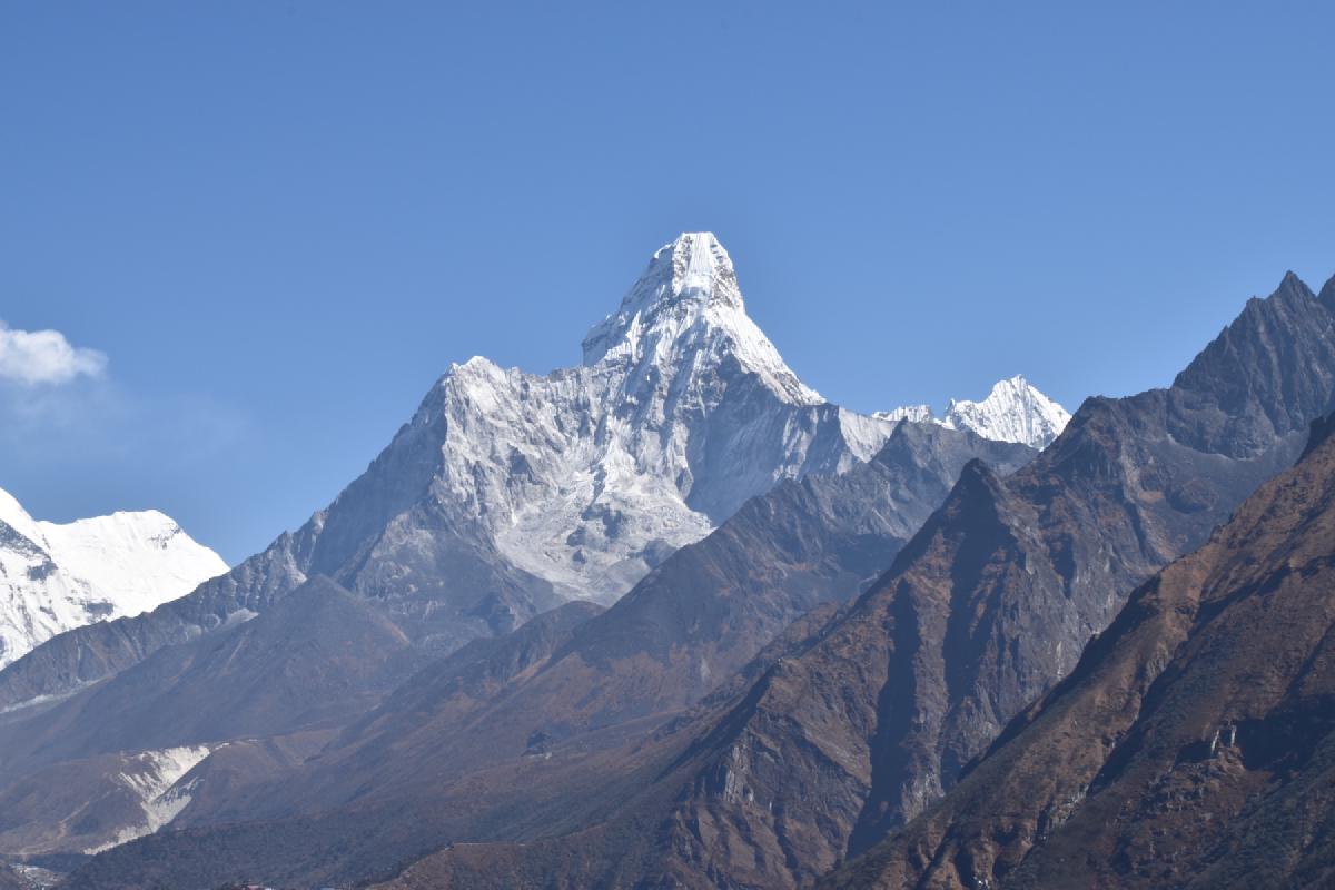 Snow-capped pyramid of Ama Dablam rising above brown ridgelines under a clear blue Himalayan sky