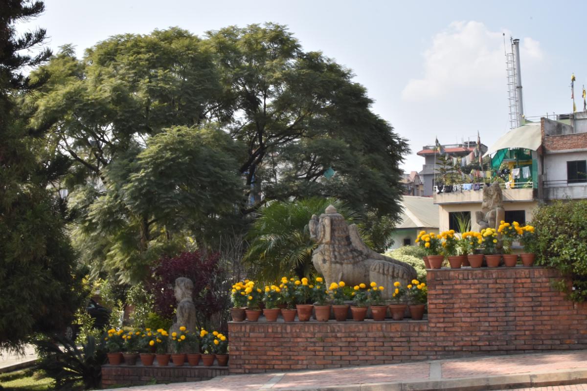 Weathered stone deity statues ringed by pots of yellow marigolds on brick terraces in a Kathmandu garden
