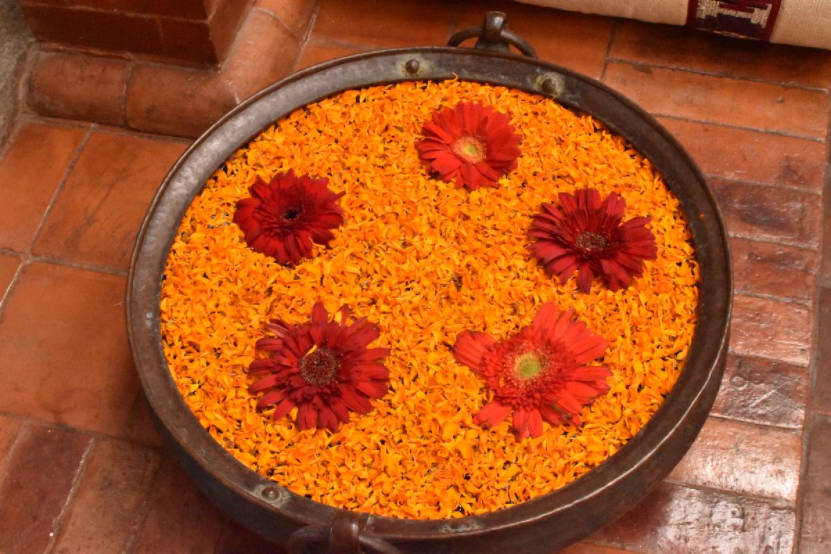 Copper basin on a tiled floor filled with orange marigold petals and five floating red gerbera blossoms